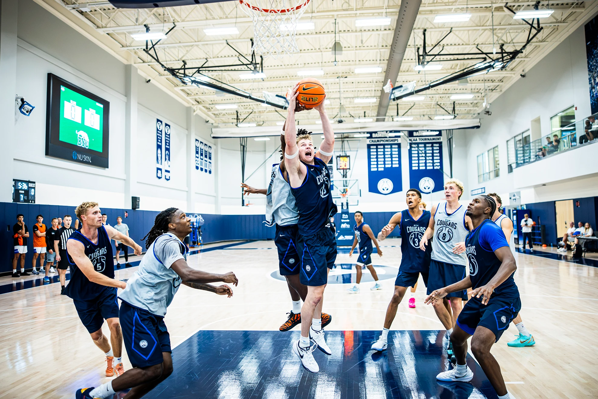 BYU men’s basketball players during a practice session, with a Cougar rising for a shot in the lane as teammates watch around the paint.